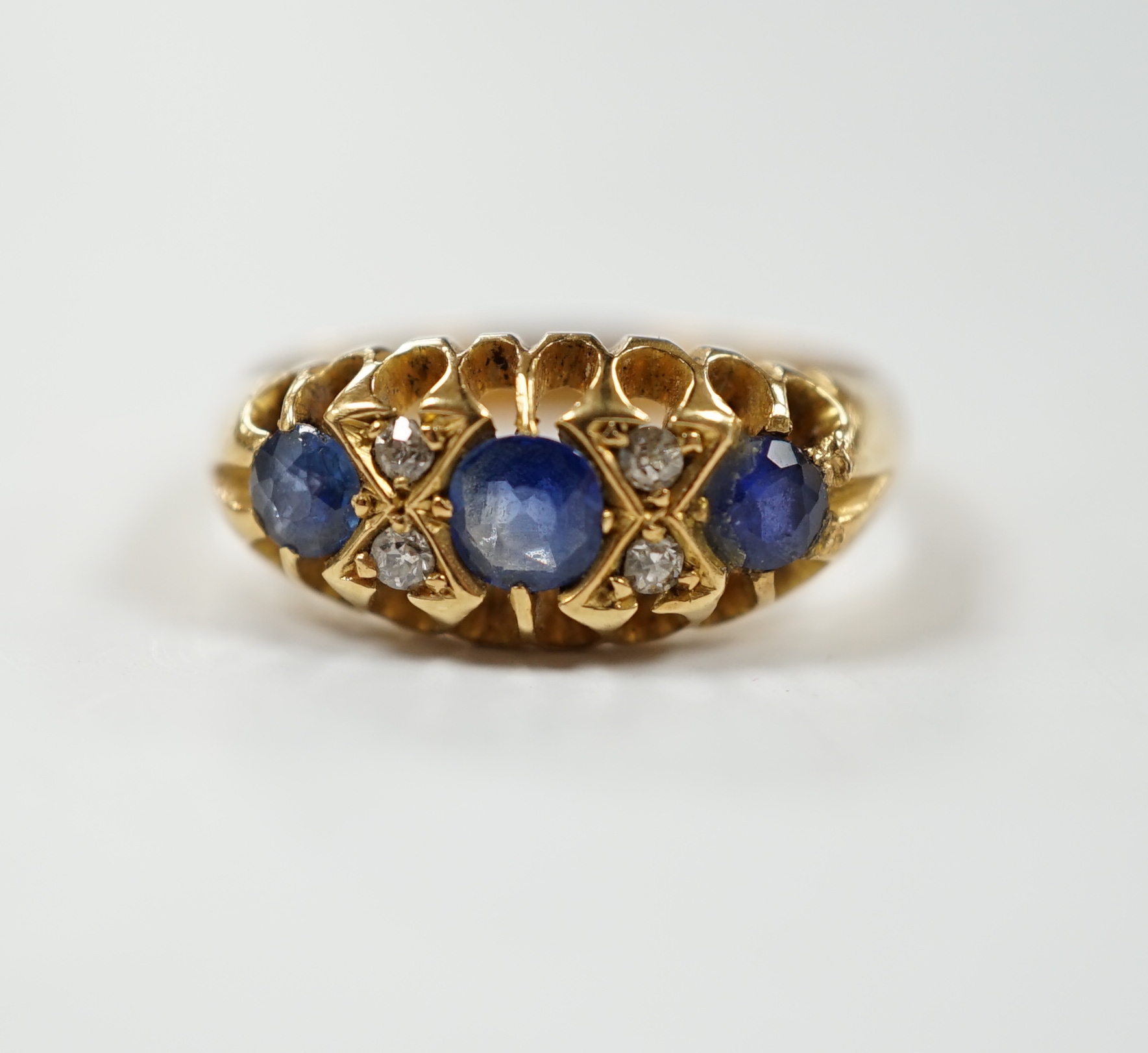 An early 20th century yellow metal, three stone sapphire and four stone diamond chip set half hoop ring, size P, gross weight 4.7 grams.